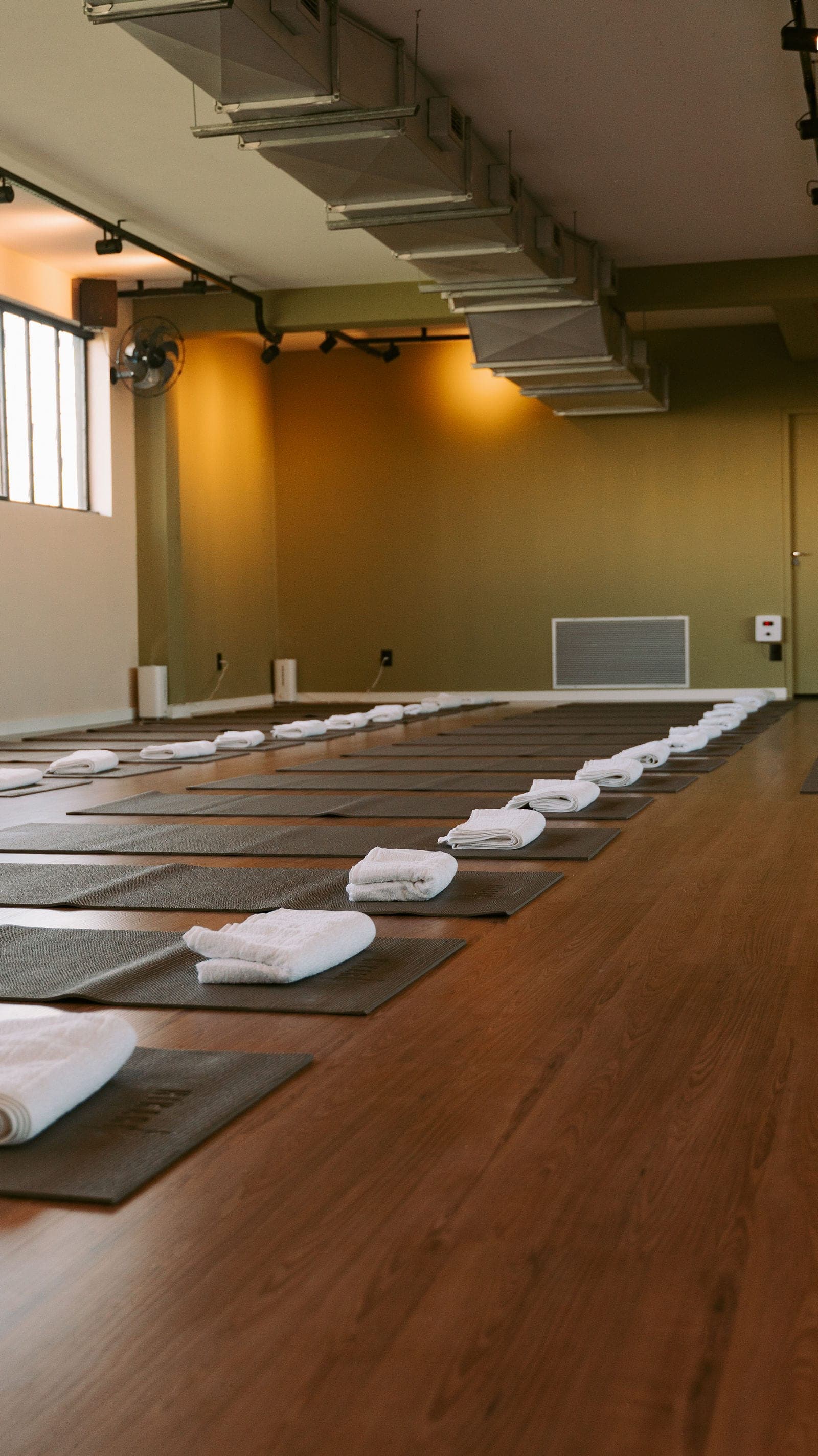 Sala de hot yoga do Hikari montada para a aula, com tapetes alinhados e toalhas brancas dobradas sobre o piso de madeira.